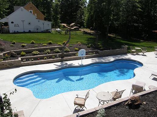 A beautifully constructed patio by patio builders surrounding a fiberglass swimming pool. The coping material, made of stone or paver, elegantly caps the edge of the pool shell, creating a seamless and visually appealing transition between the pool and the patio area.